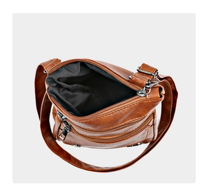 Detail of brown leather crossbody bag with multiple zippers and open main compartment
