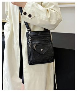Crossbody bag in soft black leather with multiple functional pockets on cream coat