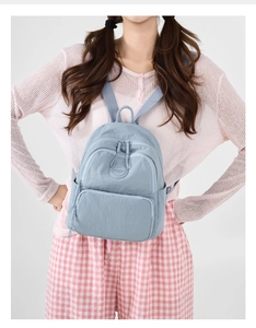 Detail of light blue minimalist backpack with multiple zip pockets and brand logo