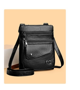 Detail of black pebbled leather crossbody bag with zipper pockets and heart metal ornament
