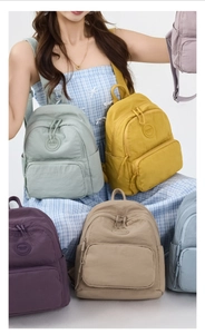 Multiple colorful nylon backpacks in green, yellow, and purple with minimalist round logo