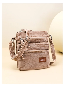Detail of vintage washed denim crossbody bag with multiple zipper pockets and logo patch