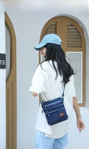 Detail of blue denim crossbody bag with triple zipper pockets and adjustable strap