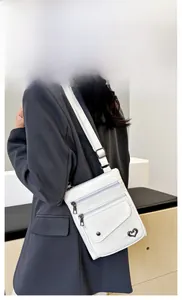 Detail view of the white crossbody bag featuring multiple zippers and a heart metal charm