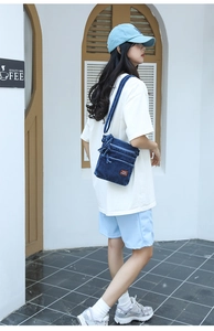 Detail of blue denim crossbody bag with multi-layer zippers and leather brand patch