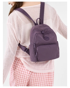 Rear view of model wearing a purple nylon backpack with logo and dual front pockets