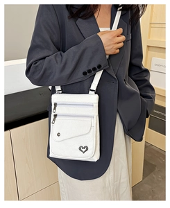 Detailed view of a white leather crossbody bag with multiple zippers on a blue suit jacket