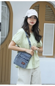 Detail of blue denim crossbody bag with multiple zip pockets and leather brand logo