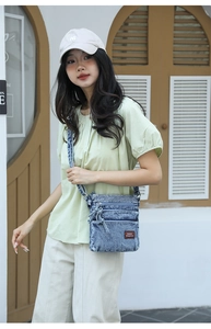Detailed close-up of blue washed denim crossbody bag with multiple zip pockets and logo patch