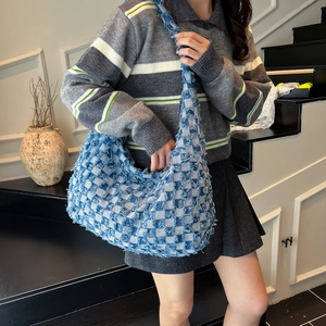 Detail of blue checkerboard denim hobo bag with frayed edges worn on model's shoulder