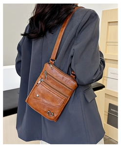 Detail of caramel leather crossbody bag featuring triple zippers and heart charm