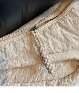 Vista macro dettagliata della borsa a pieghe in nylon crema con lungo tirante della zip intrecciato