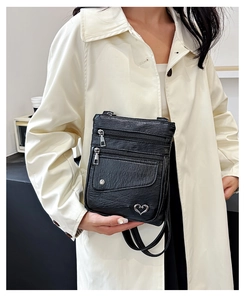 Detail view of black pebble leather crossbody bag with triple zippers and heart charm