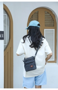 Detail of dark grey washed denim crossbody bag with multiple zip pockets and adjustable strap