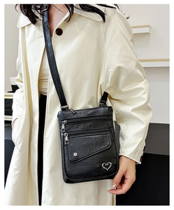 Detail of black soft leather crossbody bag with multiple zippers and heart metal accent