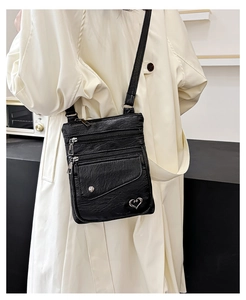 Detail of black pebbled faux leather crossbody bag with heart charm and three zippers