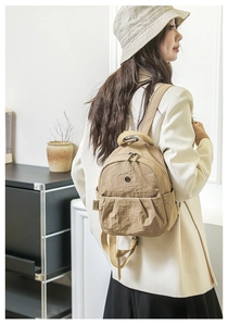 Detailansicht eines khakifarbenen Nylonrucksacks mit Faltenoptik und Trägern am Modell