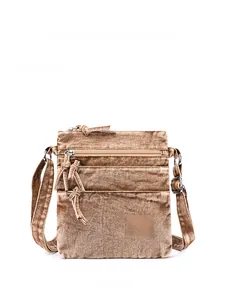 Detail of distressed brown denim crossbody bag with retro zippers and logo patch