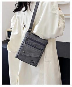 Detail of grey crossbody bag with multi-layer zippers and heart-shaped metal pendant