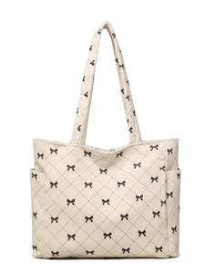 Macro detail of cream corduroy tote bag featuring black bow patterns and quilted stitching