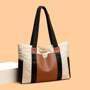 Quilted nylon tote bag with brown leather trim and shoulder strap on warm backdrop