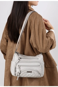 Detailed view of light gray multi-pocket crossbody bag with quilted texture on model