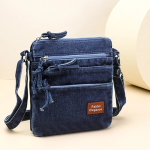 Detail of vintage washed denim crossbody bag with multiple zip pockets and leather tag