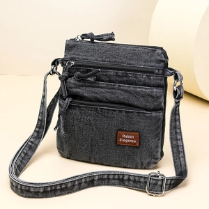 Detail of gray washed denim crossbody bag with three zipper layers and leather tag