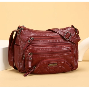 Detail view of burgundy soft leather bag showing multiple zippers and quilted front pocket