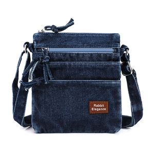 Detail of dark blue denim crossbody bag with zipper pockets and leather patch