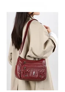 Detail view of burgundy quilted crossbody bag with multiple functional zippers on a model