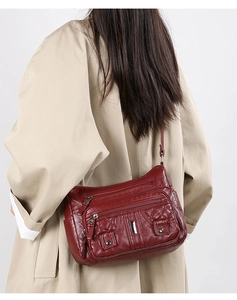Macro detail of red crossbody bag with multi-zipper pockets and polished metal accents