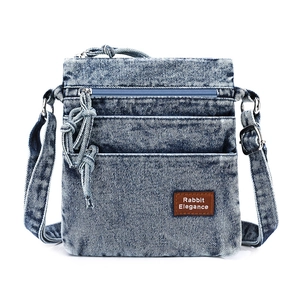 Detailed front view of blue washed denim crossbody bag with multiple layered zipper pockets