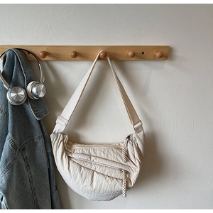 Dettaglio della borsa a mezzaluna in nylon crema con pieghe su gancio da muro minimal