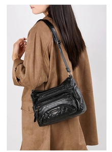 Close-up of a black washed leather multi-pocket crossbody bag worn with a casual coat