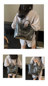 Detail of glossy black tote bag featuring white TOTE BAG text and nylon shoulder strap