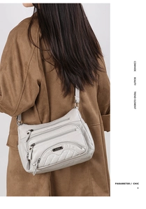 Close-up of light gray cowhide crossbody bag with multiple zippers and adjustable strap
