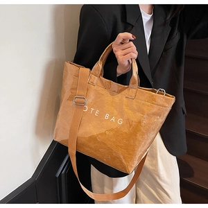 Detail of brown crinkled tote bag with white text showing strap and metal hardware