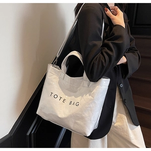 Detail of white large tote bag featuring crinkled texture and black TOTE BAG print