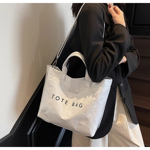 Detail of white glossy pleated tote bag with black text print worn by a model