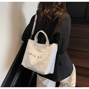 Detail view of white textured tote bag with black lettering and adjustable shoulder strap