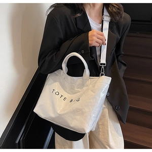 Detailed macro view of white glossy wrinkled tote bag with black minimalist text and strap