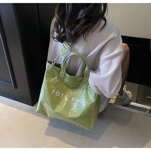 Close-up of green patent leather tote bag with fabric strap and white lettering