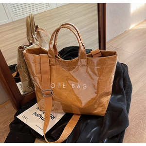 Detail of glossy brown tote bag with white text print and adjustable canvas shoulder strap