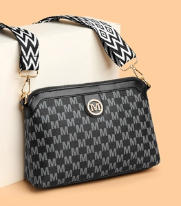 Close-up of black crossbody bag with M-pattern print and gold logo on geometric stand