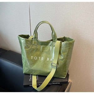 Detail of green tote bag with crinkled texture, white logo text, and canvas strap