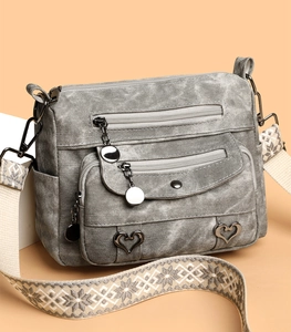 Detail view of grey washed texture crossbody bag with geometric woven strap and heart hardware