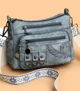 Detailed view of denim crossbody bag with multiple pockets and ethnic patterned strap