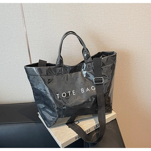 Detail of glossy black tote bag featuring wrinkled texture and wide fabric shoulder strap