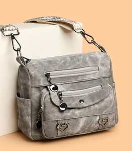 Detail of grey washed faux leather crossbody bag featuring heart buckle and woven strap